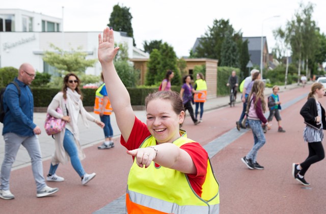 Lachende verkeersregelaar met erachter lopen kinderen en ouders