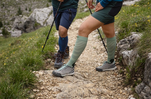 Mannen- en vrouwenbenen op een bergpad met Merino Outdoorsocks van Bauerfeind
