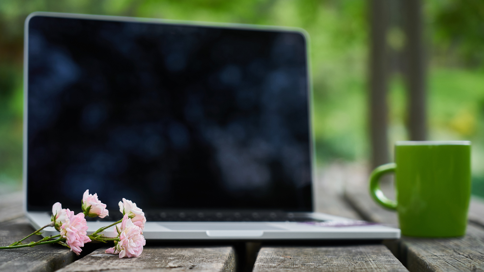 Laptop met kopje en bloemetje op houten tafel in de natuur