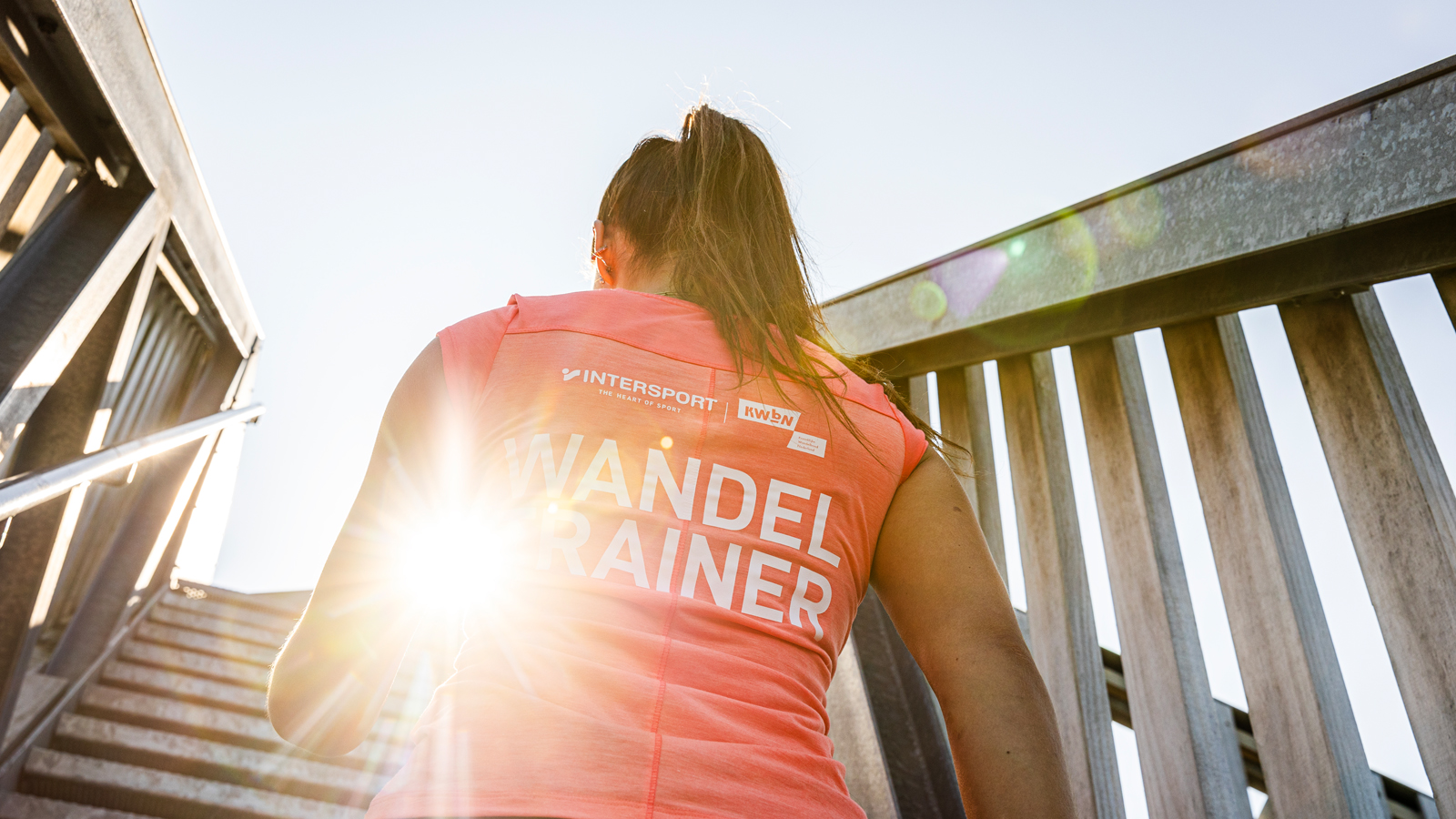 Wandeltrainer op de rug gefotografeerd terwijl ze een houten trap op loopt