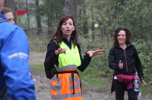 Wandeltrainer geeft in het bos uitleg aan deelnemers