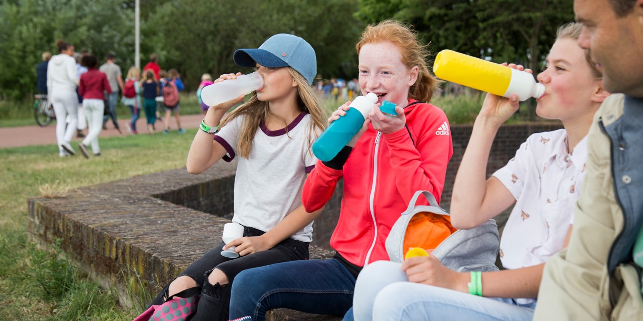 Drie meisjes op een bankje die water drinken uit een herbruikbare waterfles