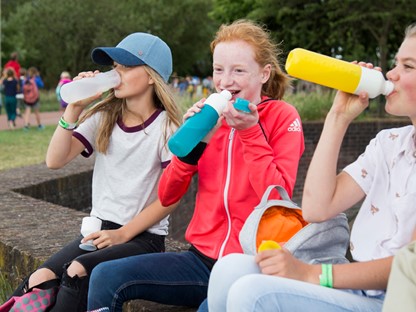 Drie meisjes op een bankje die water drinken uit een herbruikbare waterfles