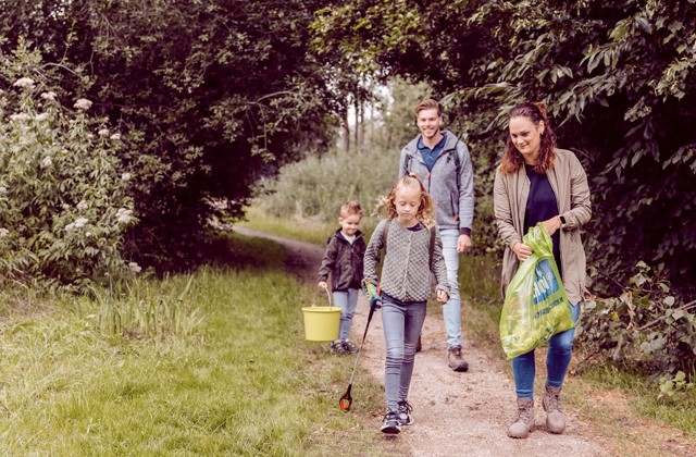 Gezin met vuilniszak en grijper wandelend in het bos