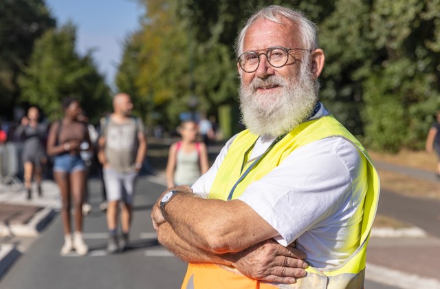 Verkeersregelaar kijkt in de camera terwijl op de achtergrond wandelaars lopen