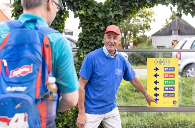 Vrijwilliger wandeltocht wijst lachend op bord met afstanden