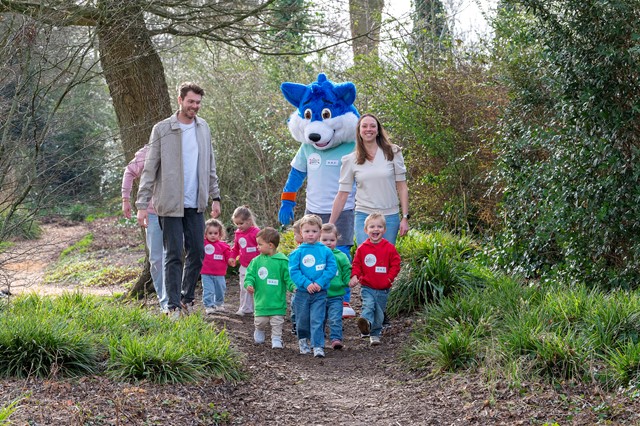 Peuters lopen samen met mascotte Fiero en twee volwassenen op een bospaadje