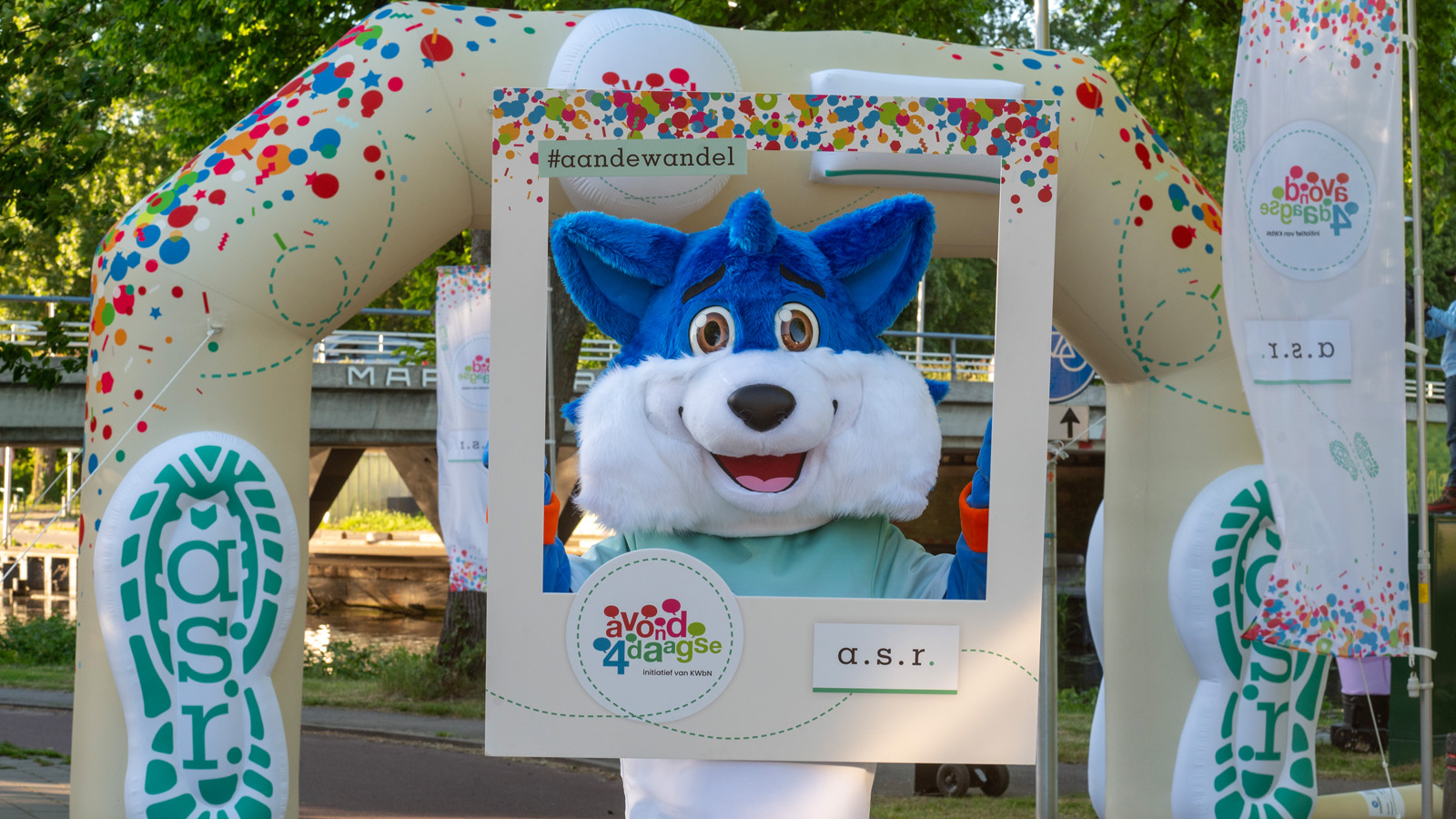 Avond4daagse mascotte Fiero onder een feestelijke startboog met een fotoframe