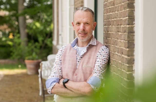 Eibert Jongsma leunt tegen muur en kijkt lachend in de camera