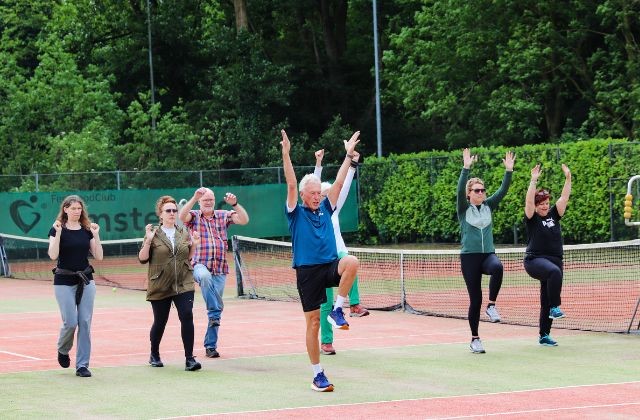 Wandelgroep doet oefeningen met trainer op tennisveld