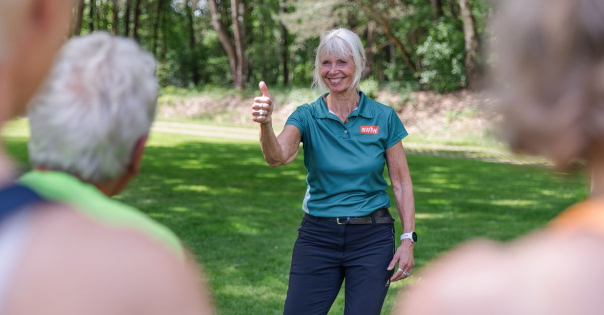 Wandeltrainer Mette van der Ven staat voor groep deelnemers en steekt duim omhoog