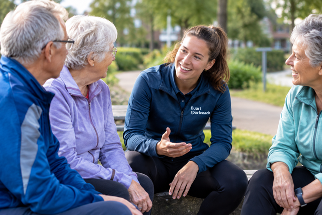 Buurtsportcoach zit op bankje en praat met drie senioren in sportkleding