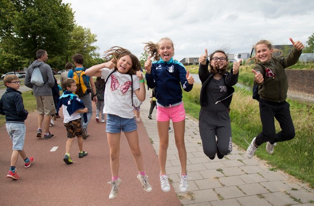 Kinderen springen omhoog tijdens de Avond4daagse en lachen en steken hun duim op